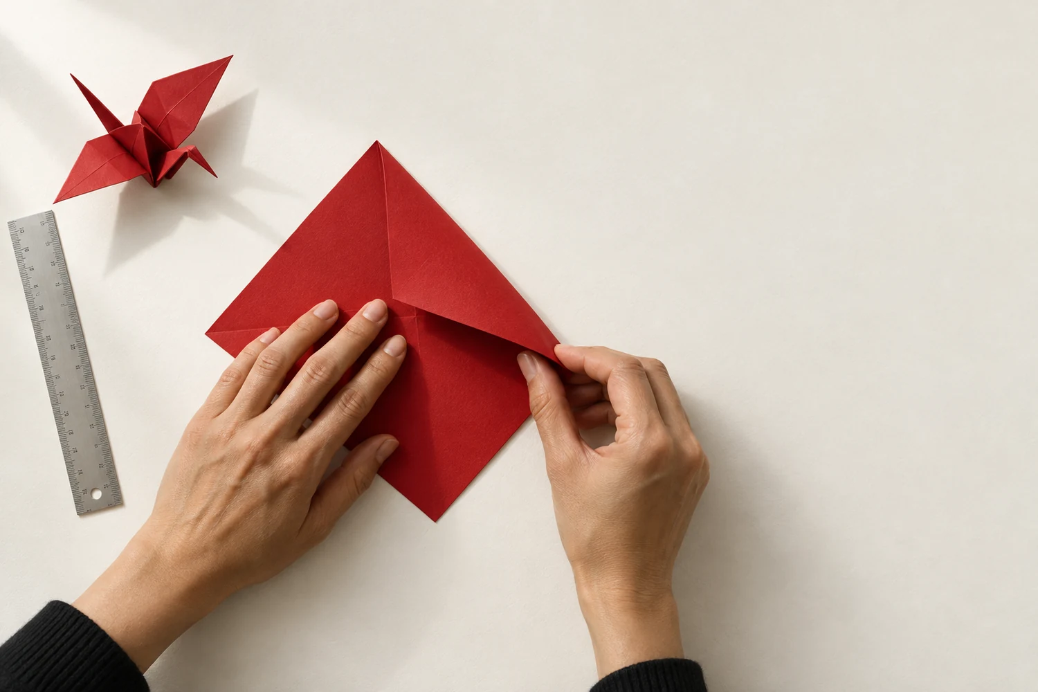 Imagen conceptual de unas manos plegando papel rojo sobre una mesa clara